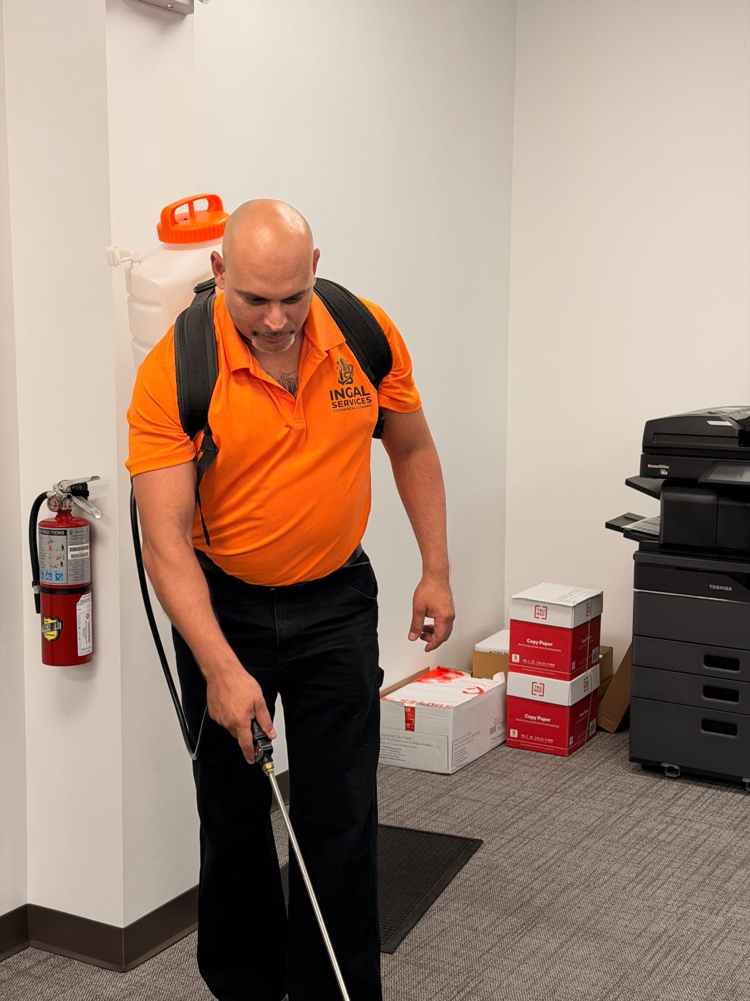 Andres, founder of INGAL SERVICES INC, applying disinfectant with a backpack sprayer at a client site
